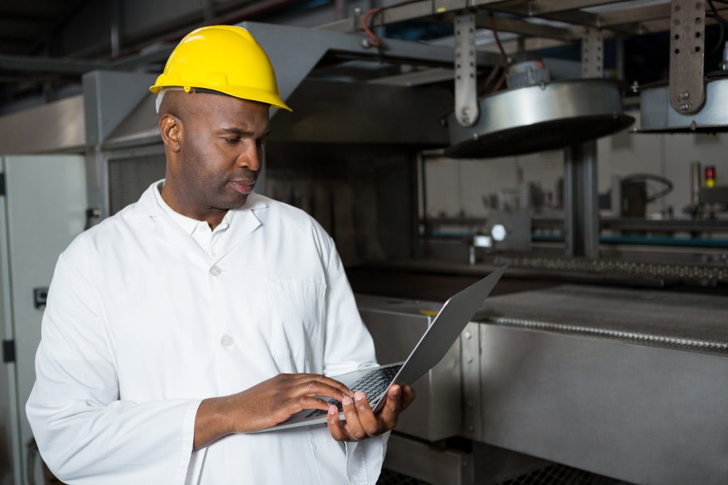 Serious male worker wearing lab coat while using laptop in juice factory